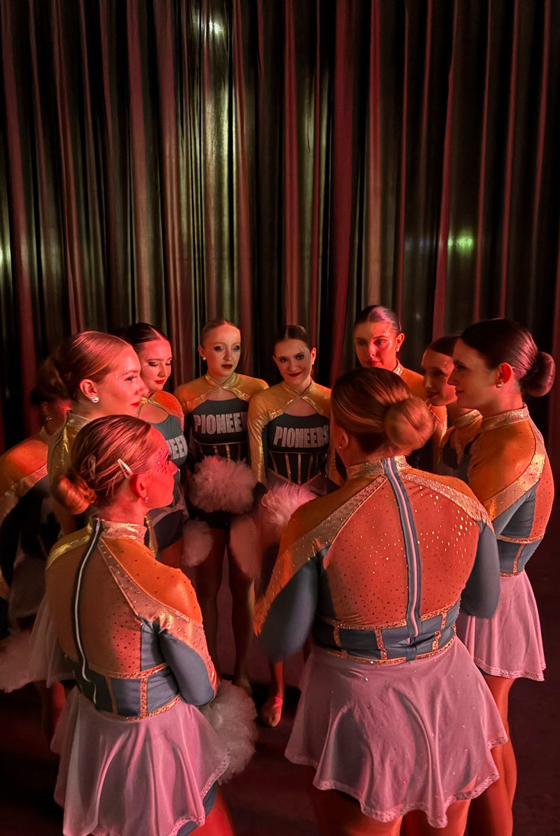 The dance team gathers in a circle in a dimly lit room.