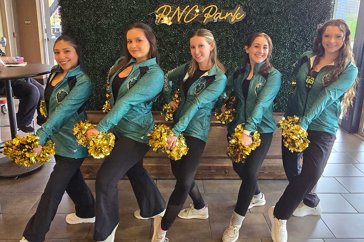 Members of the cheer team pose before a sign that reads PNC Park.