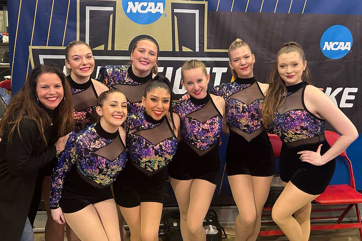 Members of the dance team pose in front of a NCAA sign.