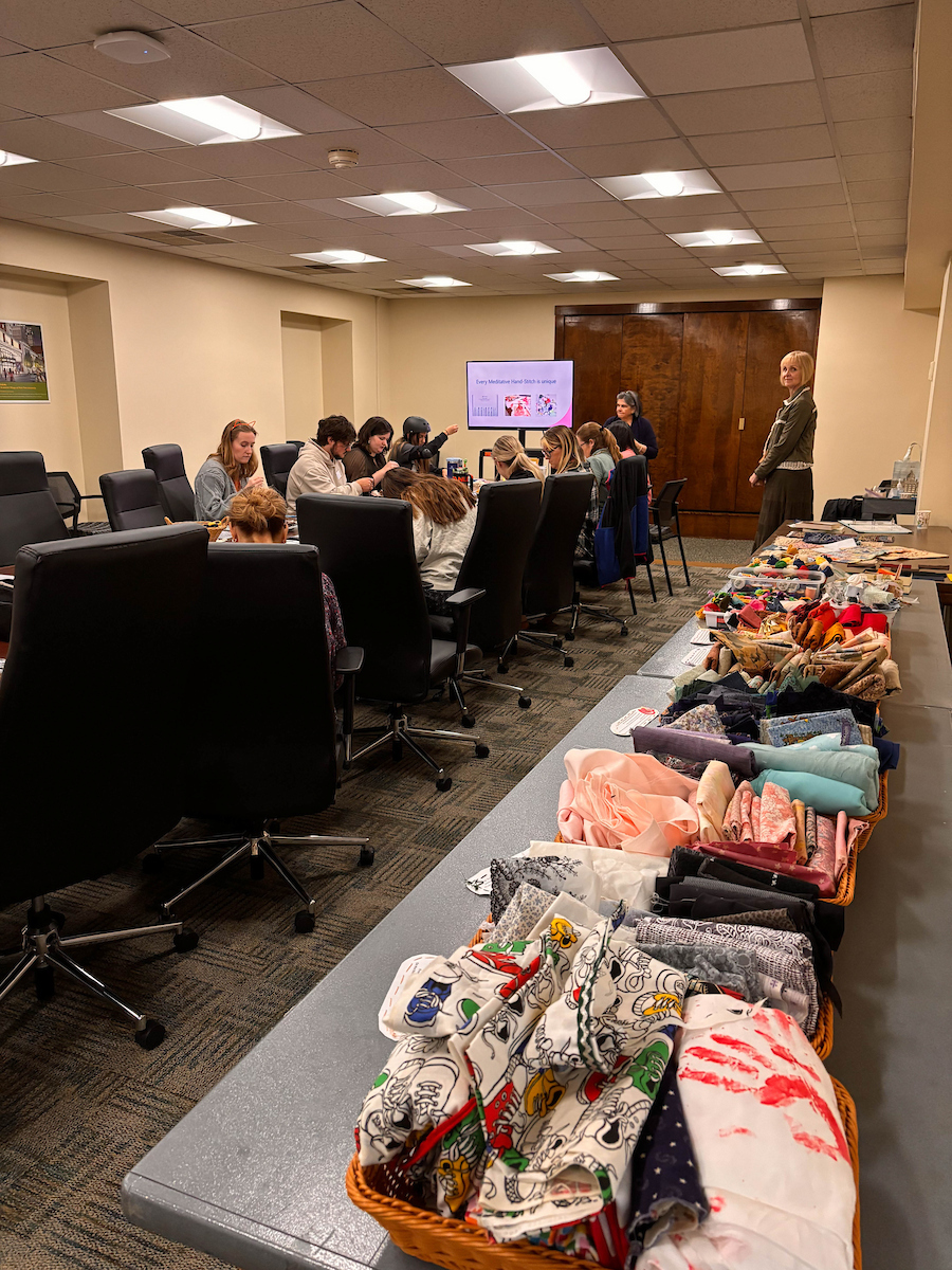 Fabric sits on a table in baskets, in the background people are taught about quilting.