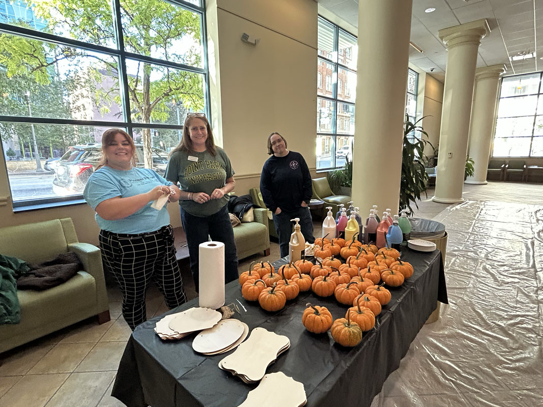 People stand behind a table of small pumpkins and paint.