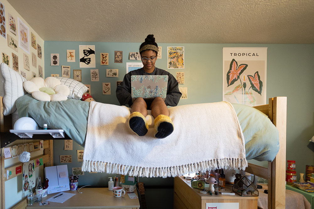 A student sits on a top bunk working on her laptop.