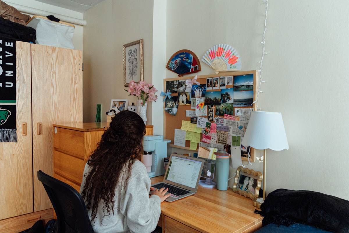 A student sits at a desk in a dorm room.