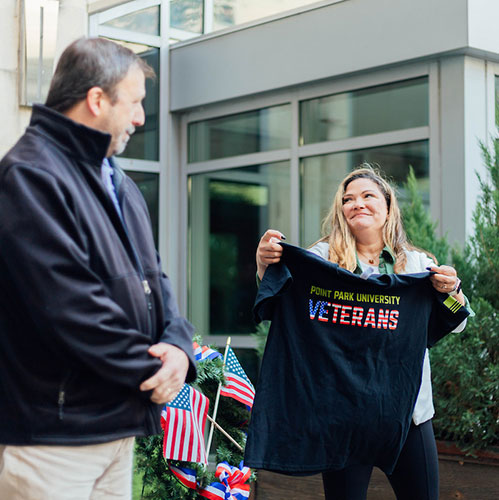 A woman presents a Point Park Veterans t-shirt to a man.