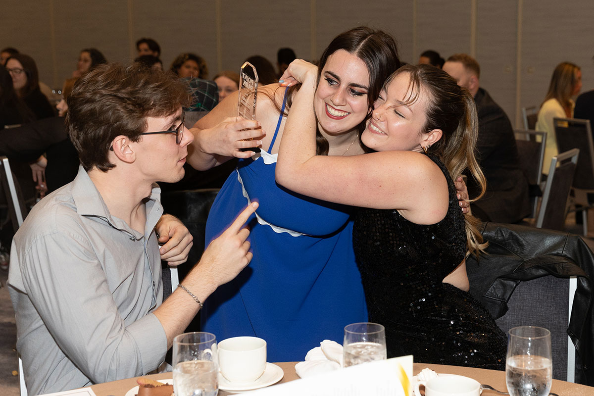 A girl holds an award and is hugged by another girl