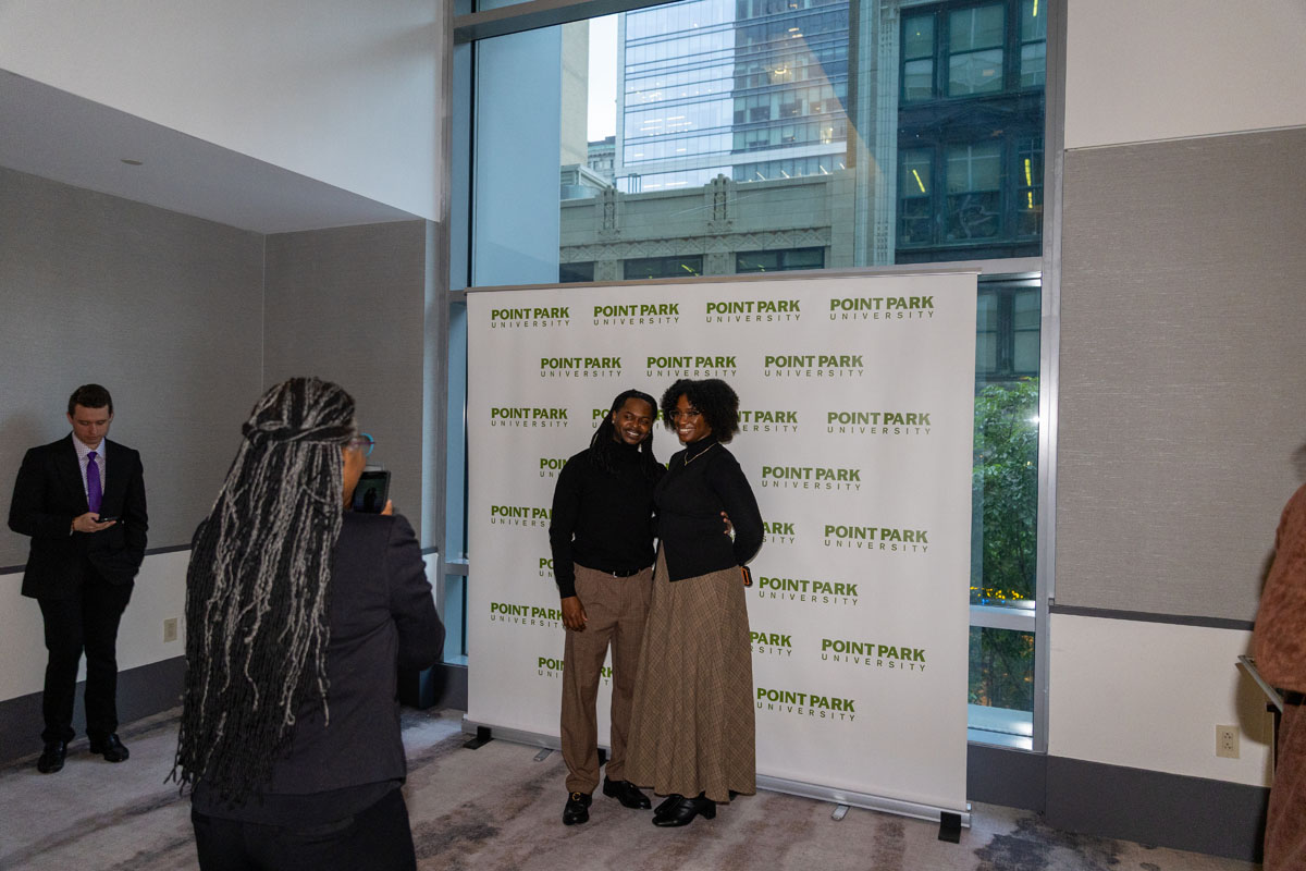 Two people get their photo in front of the Point Park banner.