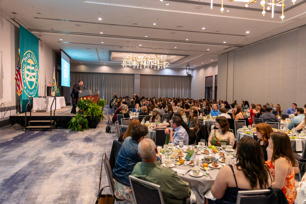 Angelo Gargaro speaks at a podium in a wide shot that shows the room full of people sitting at tables.